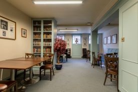 A room with several table surrounded by chairs and a large bookcase against one wall.