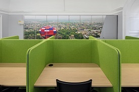 A row of desks with dividers between them. There is a row of lockers against the wall behind them.