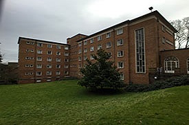 A lawn and a tree in front of a seven-storey red brick building.