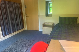 A room with a bed in one corner and a cupboard covered by curtains on the opposite wall.