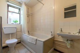 A white tiled bathroom with a toilet, a sink, and a bathtub with a shower unit and shower curtain.