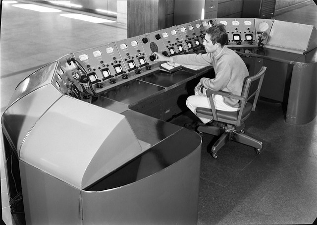 Man seated in front of old broadcasting equipment.