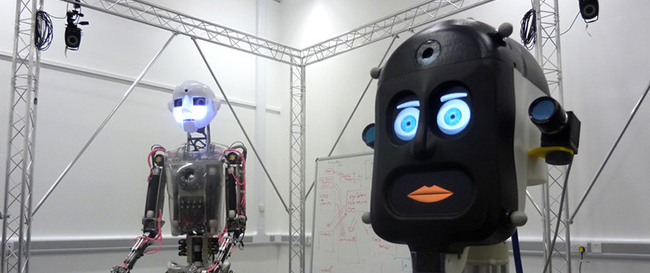 two robots in a lab, one can be seen in full in the background, and one is close up so only the face can be seen.