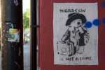 A stencil graffiti on a wall of Paddington Bear walking with his suitcase, accompanied by the words 'Migration is not a crime'.