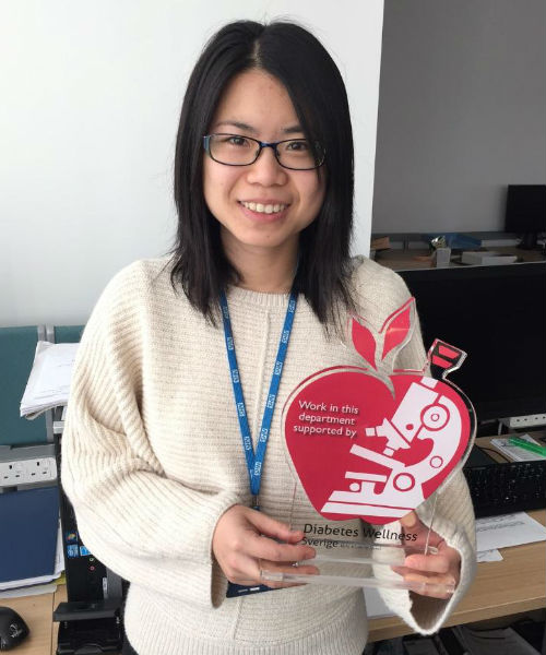 A smiling student holding up a heart shaped plaque.