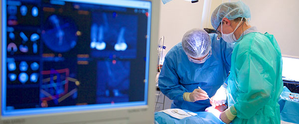 A screen showing x-rays, with students operating on patient in the background.