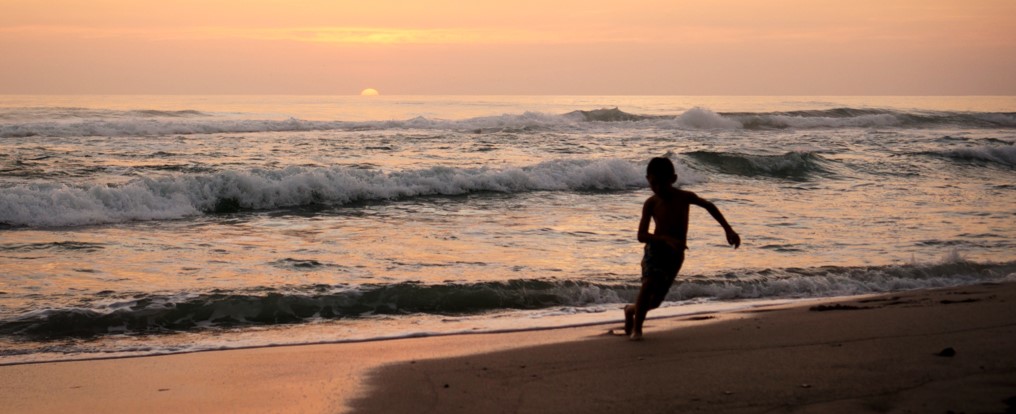 A child plays in the waves on a Costa Rican beach at sunset
