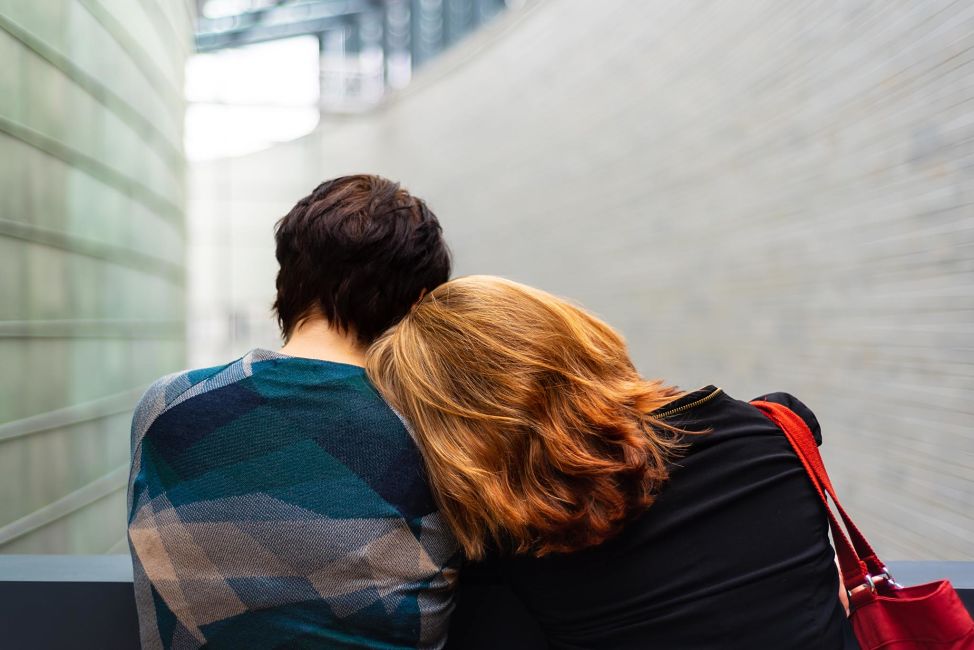 Two women sitting side by side, one puts her head on the other's shoulder