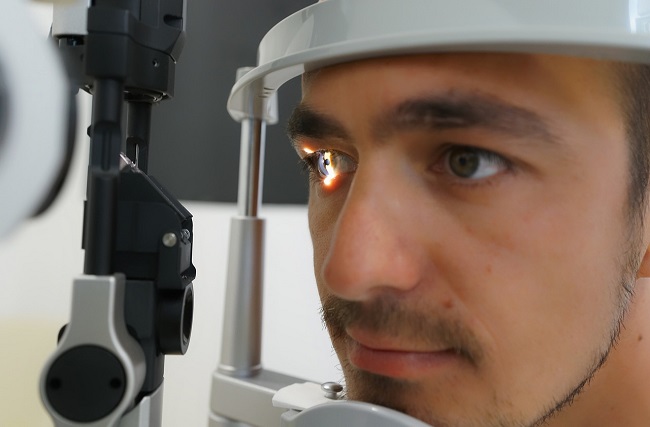 Man having an eye examination resting chin on machine as light is shone into one eye.
