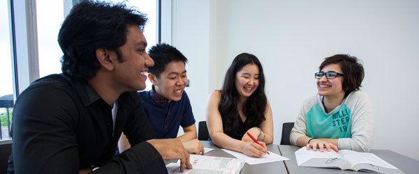 Four men and women of different races sit around a table laughing as they work together. 