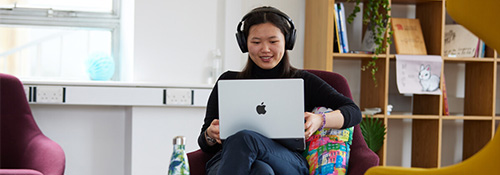 a student sat with their laptop wearing headphones and smiling in conversation