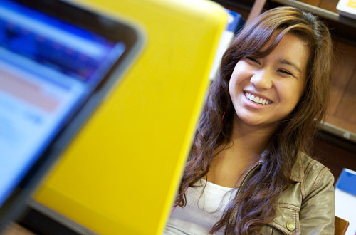 A student smiling at their laptop screen.