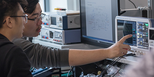 Two people pointing at the screen on a piece of of engineering equipment. 