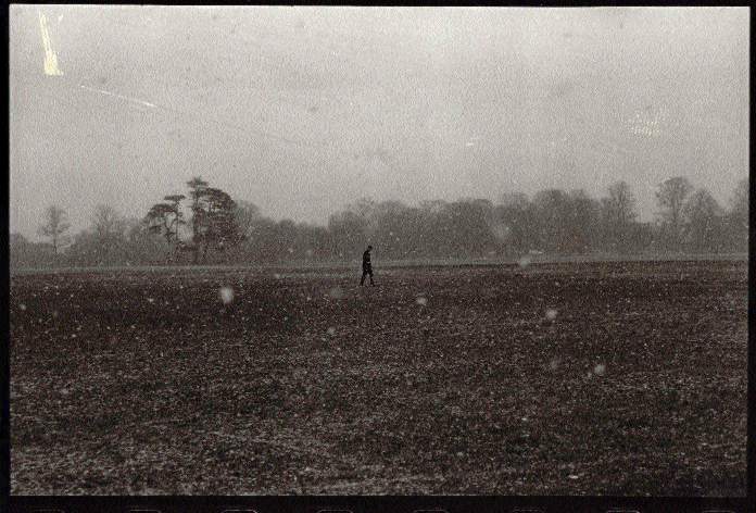 photograph of a figure in a field, during snowfall
