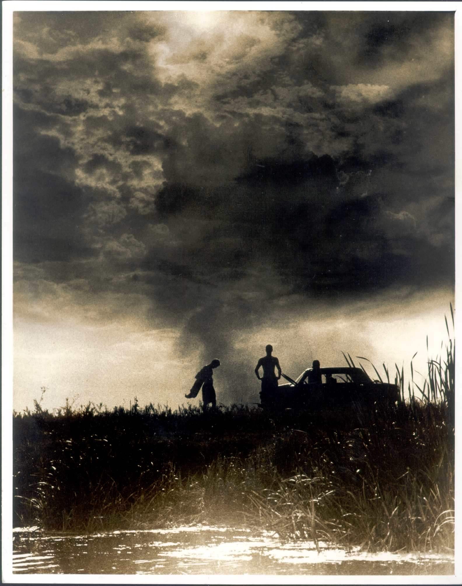 photograph of three boys and a car set against the sky