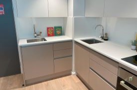 A corner kitchen unit with grey cupboards. There are two sinks with taps. 