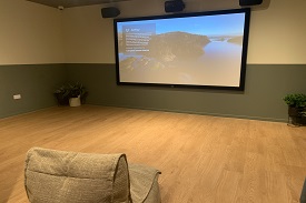 Comfy seat in the foreground. Screen in the background of the cinema room.