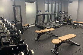 Gym area with weights to the left and running machines in the background on the right and benches in the foreground.