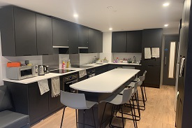 Kitchen table in the foreground with chairs and kitchen cupboards and appliances in the background.