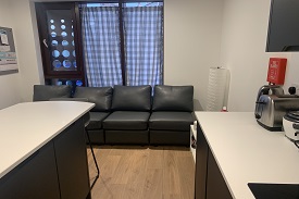 Kitchen table to the left and kitchen cupboards to the right. In the background is the window and below it is the sofa.