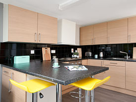 A kitchen with a sink, and oven and hop, lots of cupboards, and two chairs at the kitchen counter.