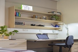 A desk with an office chair beside it, drawers beneath it and shelves above it.