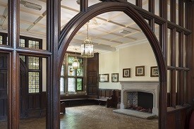 A hallway with wooden doors and panels, and fireplace and stained glass windows.