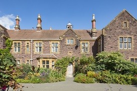 Exterior of a large three-storey red brick redidential building, with a garden in front of it.