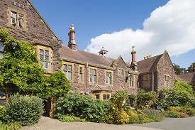Exterior of a large three-storey red brick redidential building, with a garden in front of it.
