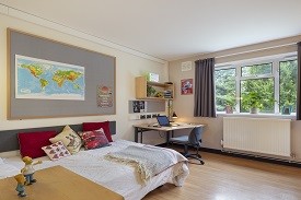 A room with a single bed in one corner and a desk with an office chair in another corner. The desk has two shelves above it.