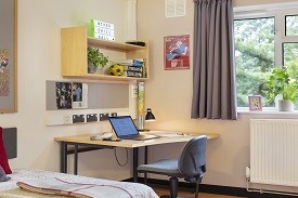 A desk in the corner of a room, with an office chair nearby and shelves above it.