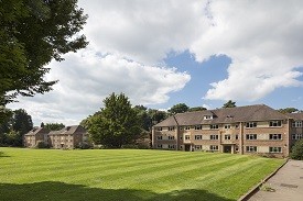 Exterior of two large four-storey red brick redidential buildings, with a lawn in front of them.
