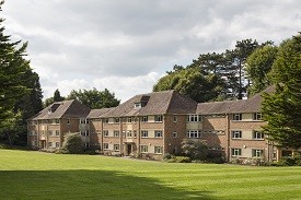 Exterior of a large four-storey red brick redidential building, with a lawn in front of it.