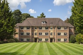 Exterior of a large four-storey red brick redidential building, with a lawn in front of it.