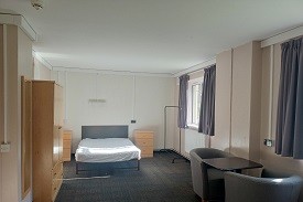 A 4ft bed in the background, wadrobe to the left and windows to the right with  two chairs and a table to the right.