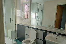 Shower cubicle to the right of the bathroom. Toilet to the right of the shower and basin to the right of the toilet. Large mirror on the back wall.