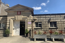 Exterior of a single-story sandstone building. There are potted plants near the entrance.