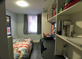 A bedroom, with bed, desk, chair and shelves