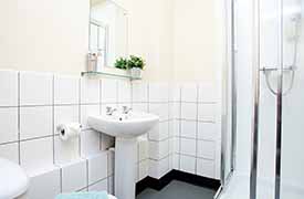 A bathroom with a toiler, sink, mirror and shower cubicle.