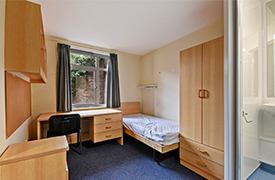 A bedroom with a single bed, a desk and office chair next to it, and a cupboard at the foot of the bed.