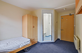 A bedroom with a single bed, a cupboard, and a doorway into an ensuite bathroom.