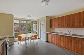 A kitchen with a dining table and four chairs, and oven, two sinks and lots of cupboards.