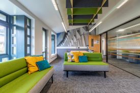 A room with two sofas, a table with six chairs, and a glass wall showing the corridor outside.