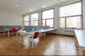 A room with four long desks. There are dividers in the middle of some of the desks, and some chairs at the desks.