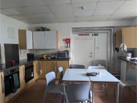 A dining area with tables and chairs, fitted cupboards, ovens, and kitchen appliances.