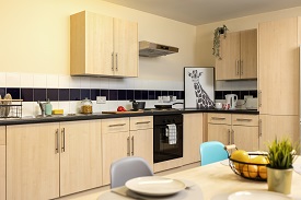 Wooden kitchen units that include a cooker, sink, drainer, storage cupboards, dining table with plates, fruit and a plant on it.