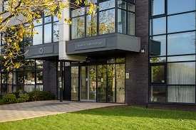 Entrance to building which has automatic doors. Concrete pathway leading to building with grass on either side of pathway.