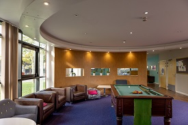 Room with comfy chairs and sofas on the left hand side with a pool table in the centre of the room.