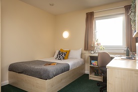 A double size bed with a soft light above the bed and a corner desk and chair to the right hand side.