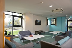A room with comfy tables and chairs and a tv mounted on the back wall.